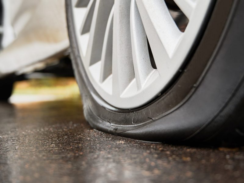 Close-up view of punctured, flat tire on rear wheel of automobile. Fault, damage wheel while driving on asphalt road. Bad luck, accident concept.